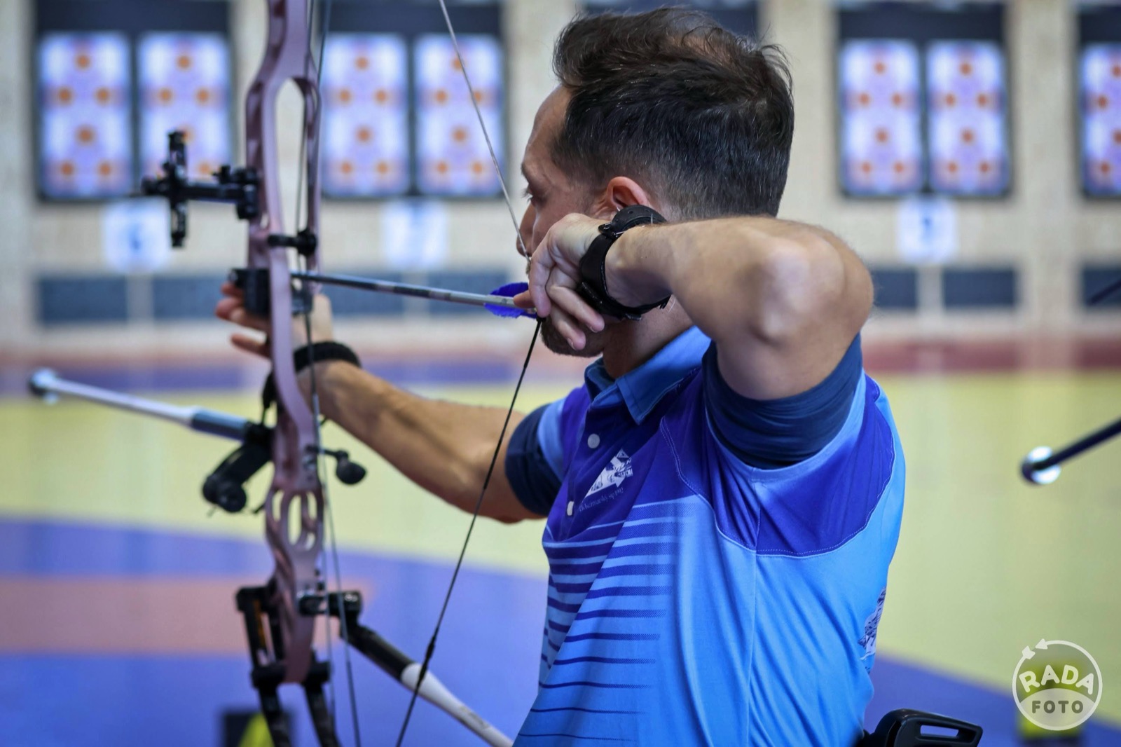 Roman Bekeš mieri kladkovým lukom počas halovej súťaže, detailný záber na sústredenie pri výstrele
